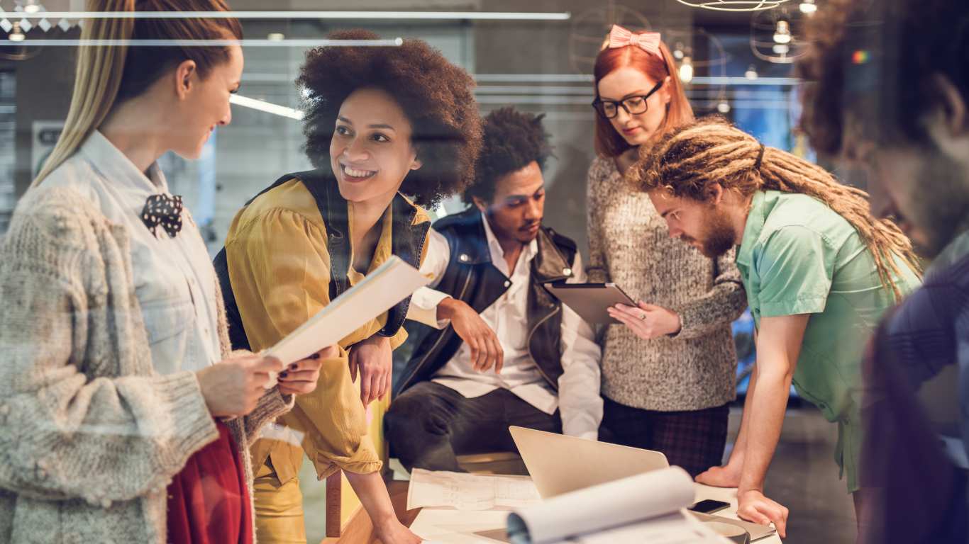 A diverse group of professionals collaborating around a table in a modern workspace, engaged in creative problem-solving and teamwork. The image highlights energy, connection, and innovation in a corporate setting.