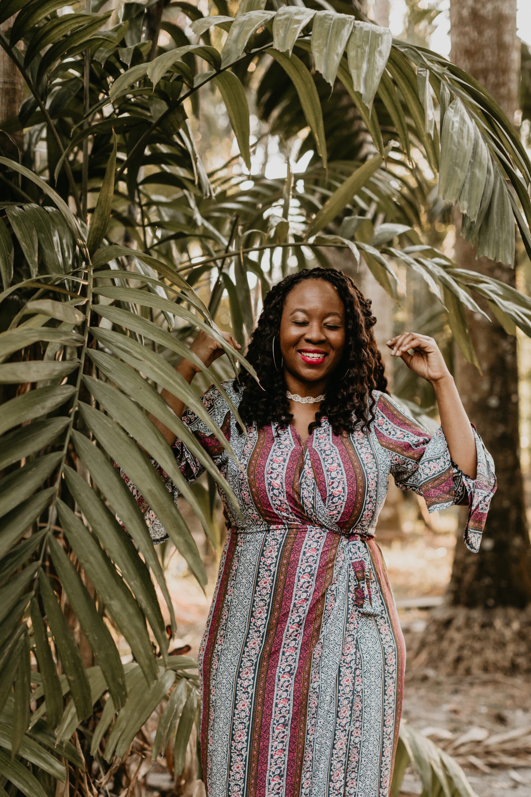 A vibrant woman standing amidst lush tropical greenery, wearing a colorful patterned dress and radiating joy with a serene smile. The image captures a sense of harmony, resilience, and connection with nature.